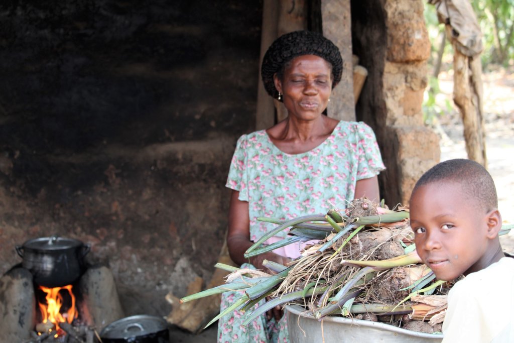 This photo shows a lady and her grandson boiling water in a pot over an open fire