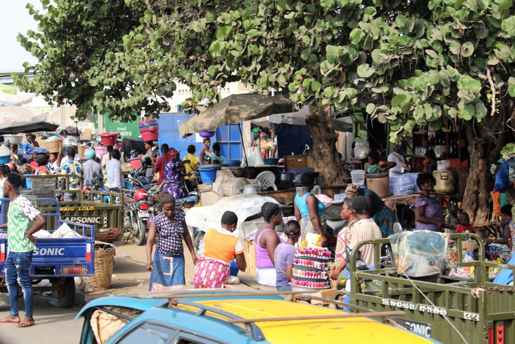 This photo shows lots of people, cars and stalls on a busy street in Lome