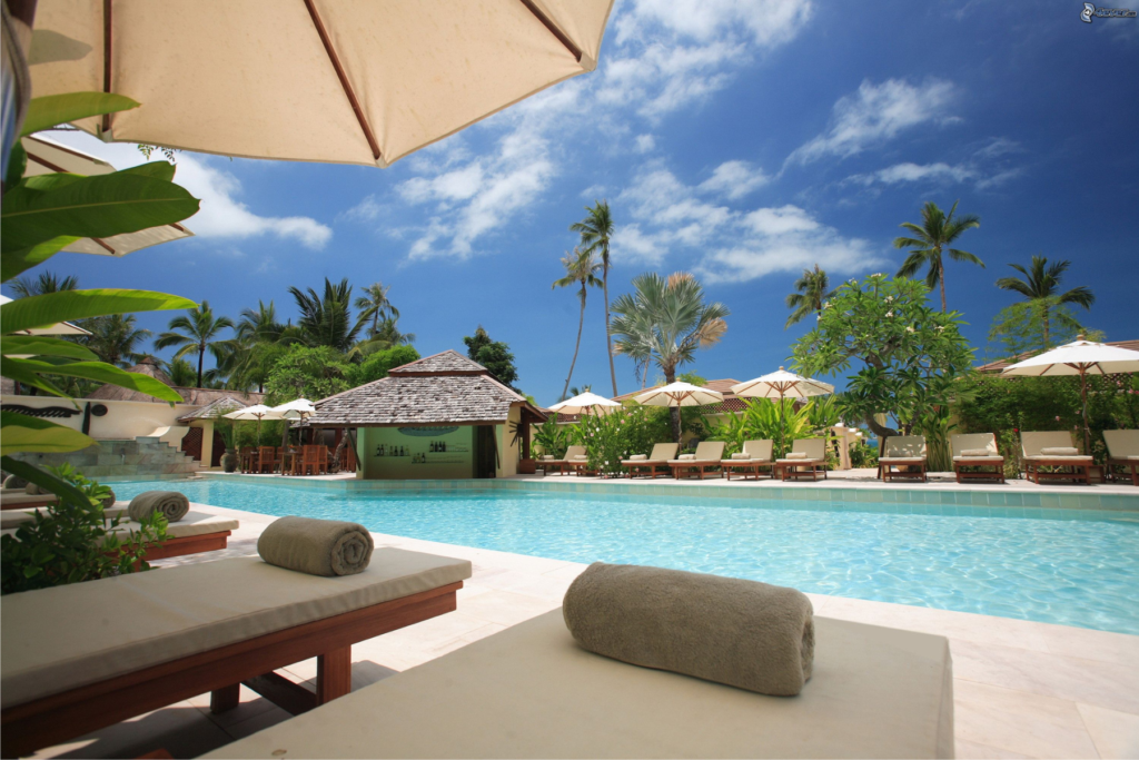 This photo shows sun loungers arranged around a pool. The sun is shining and the sky is blue.